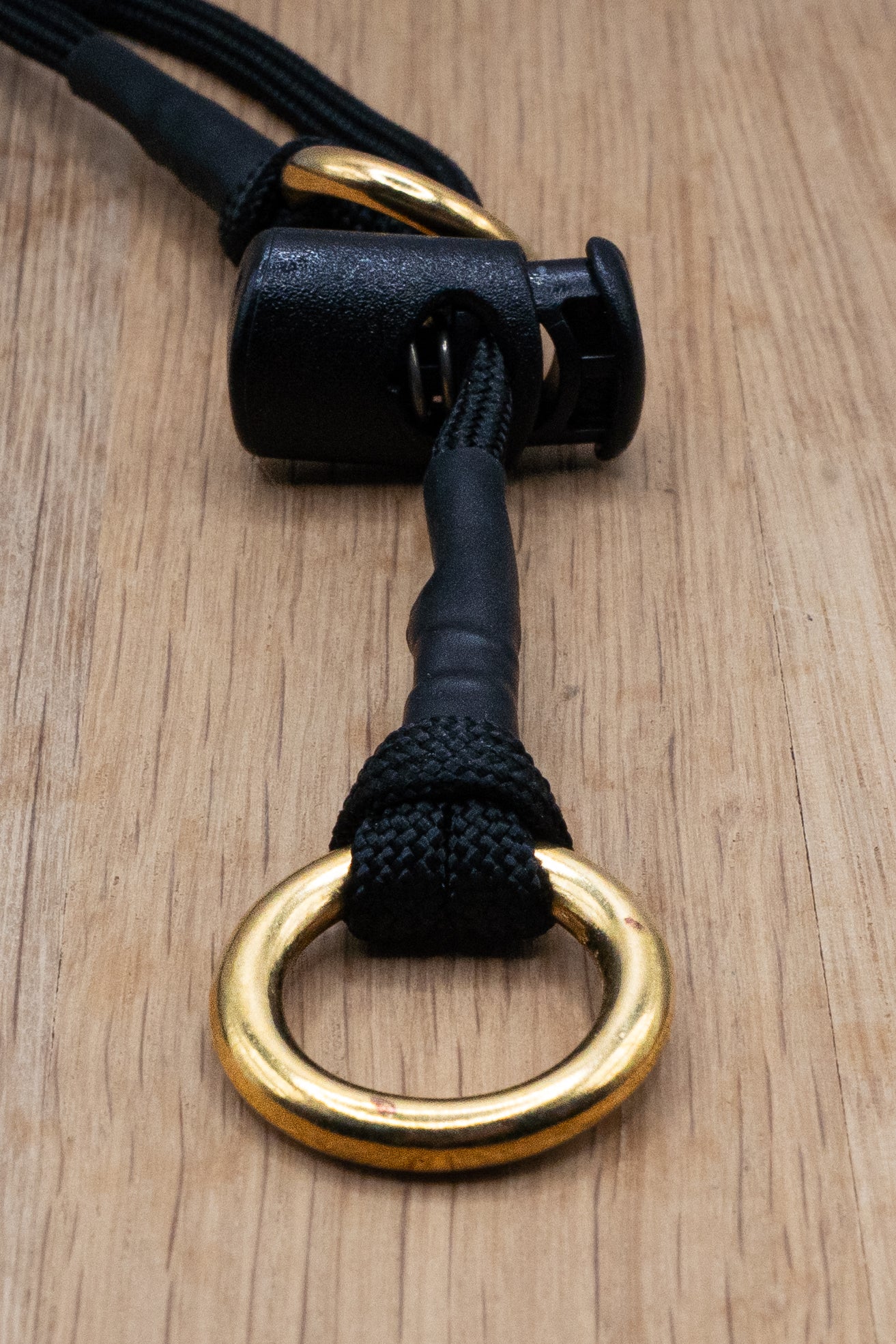 Black paracord attatched to a solid brass 16mm 'O' ring featuring a cord stopper.