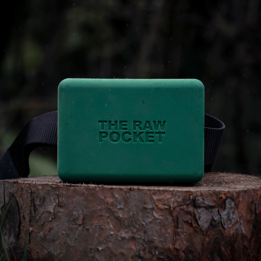 A green silicone treat pouch The Raw Pocket shown on a stump with a belt.